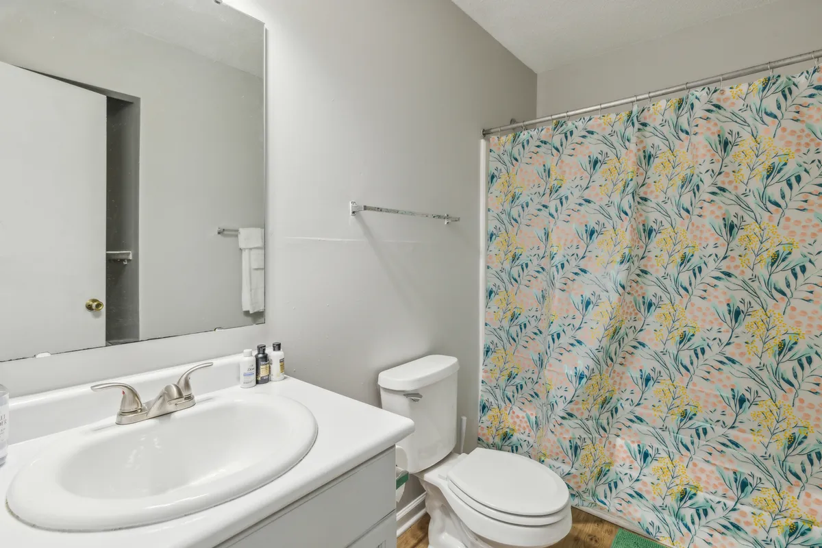 An inviting bathroom featuring a sink, shower curtain, and mirror. The layout is practical yet serene, providing a sense of privacy and relaxation ideal for personal grooming or unwinding at the end of the day.
