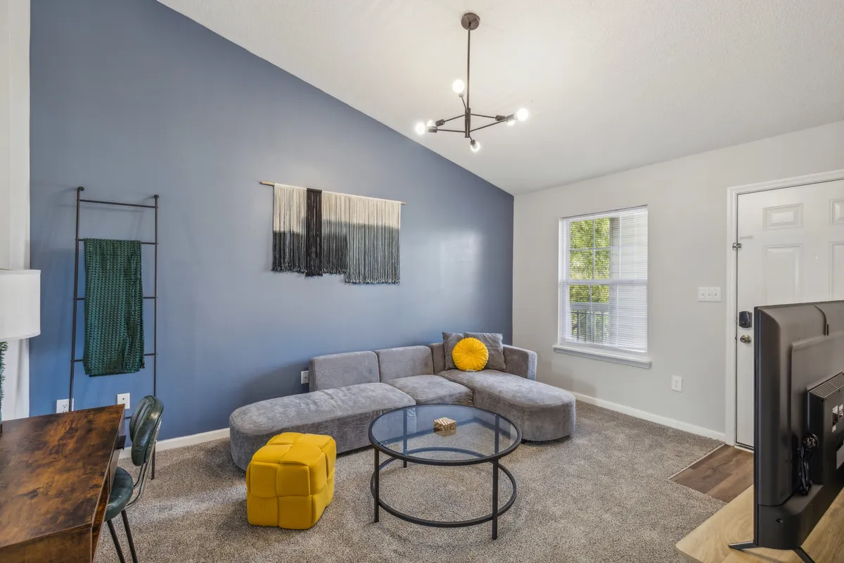 The image showcases a stylish living area featuring a plush sofa, a cheerful yellow pouf, modern artwork on the wall, and a chic coffee table. The arrangement is inviting and ideal for relaxing, entertaining, or enjoying a quiet morning coffee.