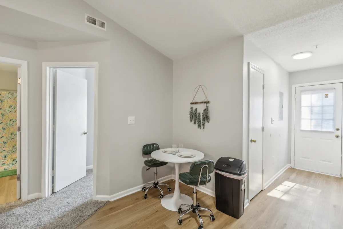This image presents a small round dining table with green chairs, set in an intimate corner near a doorway. The area feels cozy and functional, ideal for shared breakfasts, quick meals, or casual conversations.