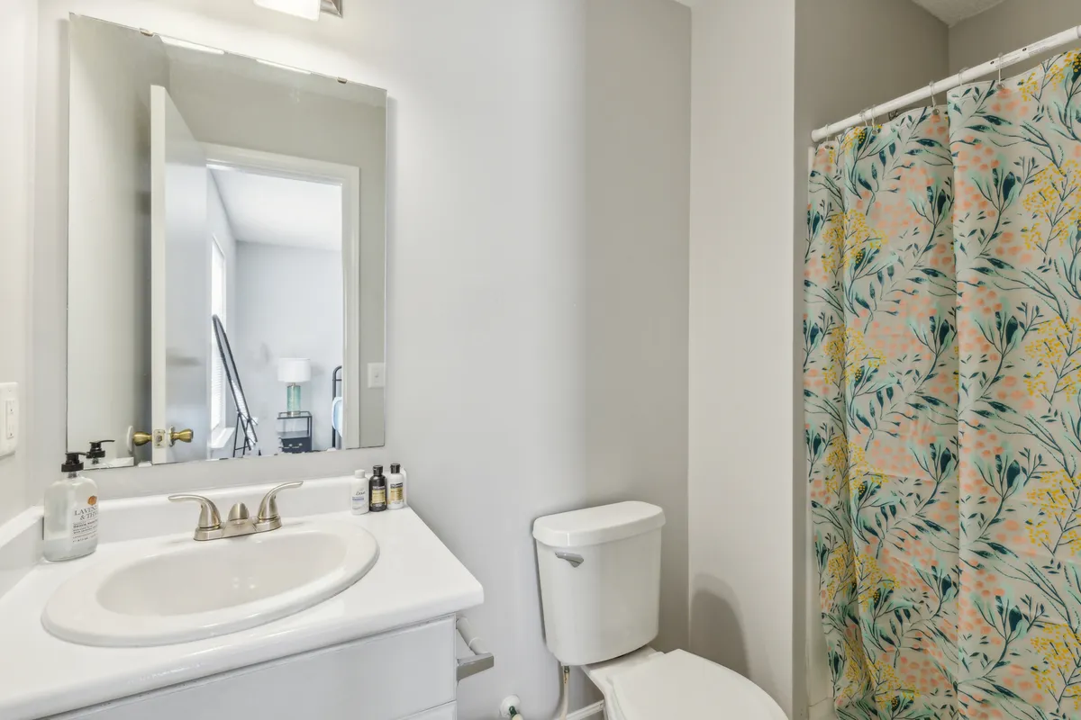 This bathroom showcases a vanity with a sink, a colorful shower curtain, and a bright mirror reflecting light. The space feels fresh, clean, and designed for morning routines or relaxing refreshing showers.